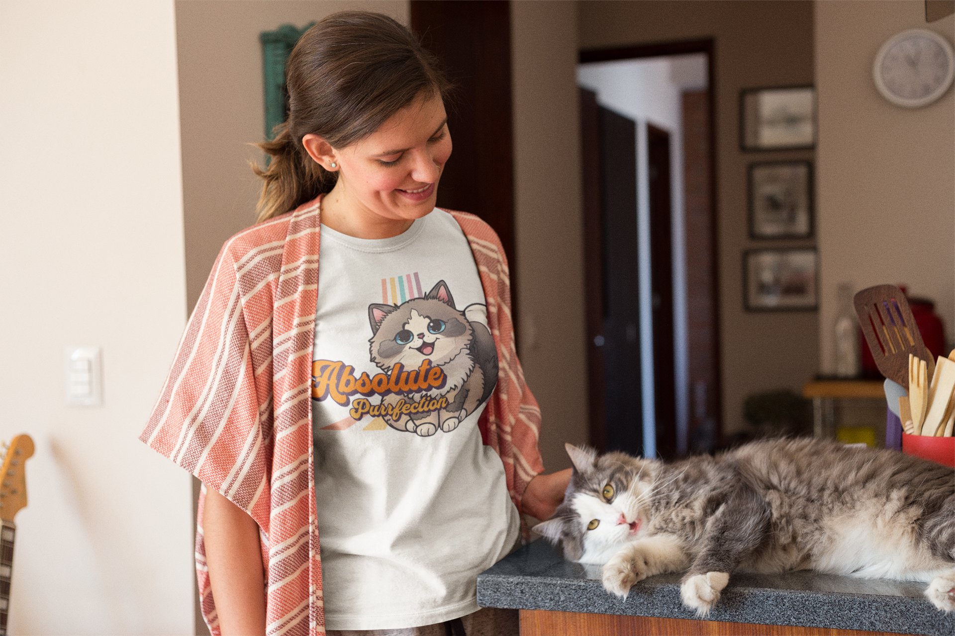 Woman wearing an Absolute Purrfection tee, smiling as her cat lounges beside her
